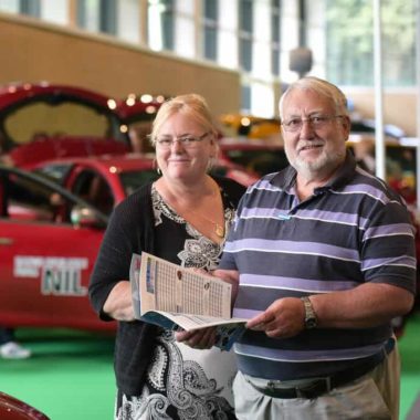 Female and male couple at car show smiling and holding the event guide